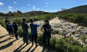 the San Diego Coastkeeper team stands before a pile of trash in Smugglers Gulch, pollution from the Tijuana River Sewage Crisis. 